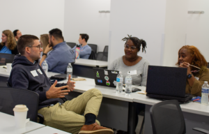 SAQ Fellows sit at a long white table and engage in conversation.