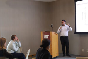 Chris Campos presents behind a podium while audience members watch. 